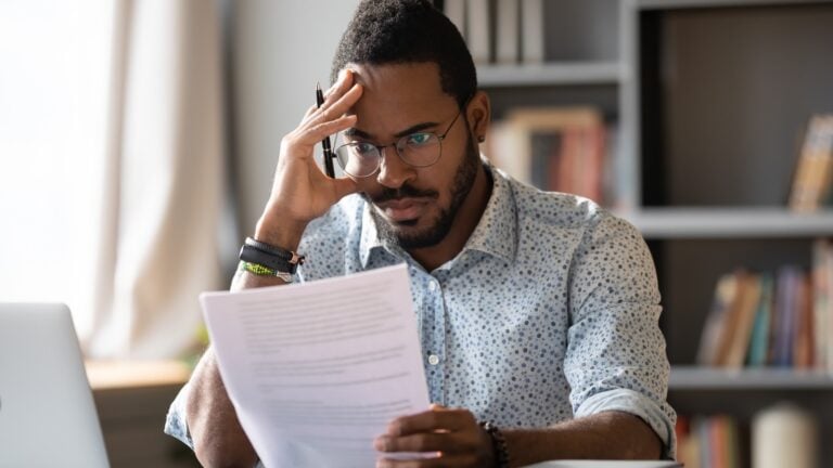 A person carefully reviewing a printed letter beside a laptop.